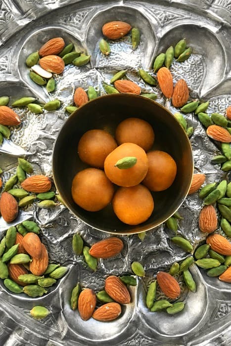 Microwave Besan Ladoo on a large silver ornate plate with almonds and cardamom pods