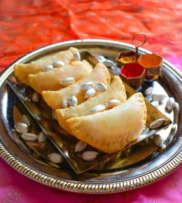 Gujiya or Karanji on a metal plate with cardamoms