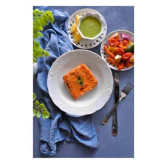 tandoori salmon on a white plate with vegetables on side