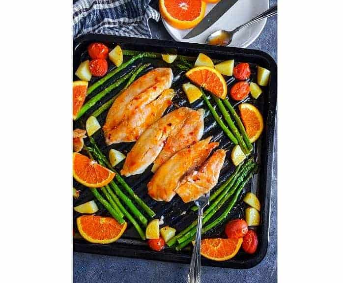 orange ginger glazed tilapia fish with vegetables on a black oven tray.