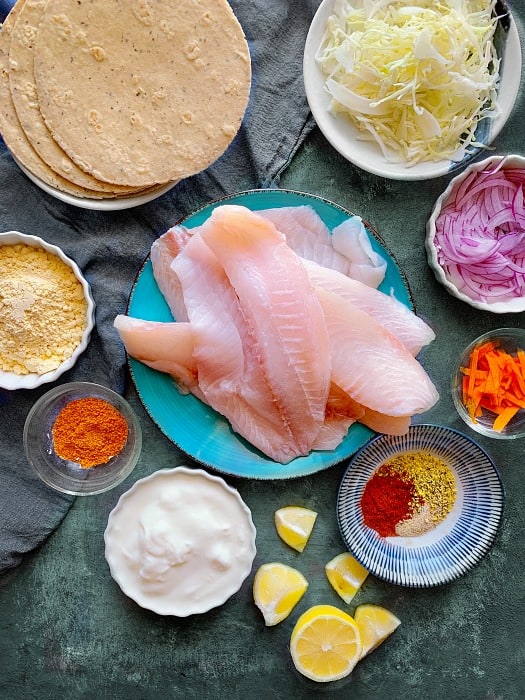 Tandoori Fish Tacos ingredients like fish, tandoori spices, yogurt, cabbage, onions on blue platter